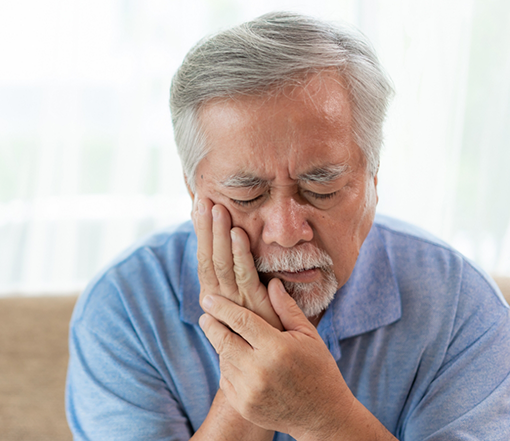 Man holding his cheek in pain before seeing an emergency dentist in Forest Grove