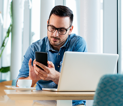 Man using his phone while sitting at a table with a laptop